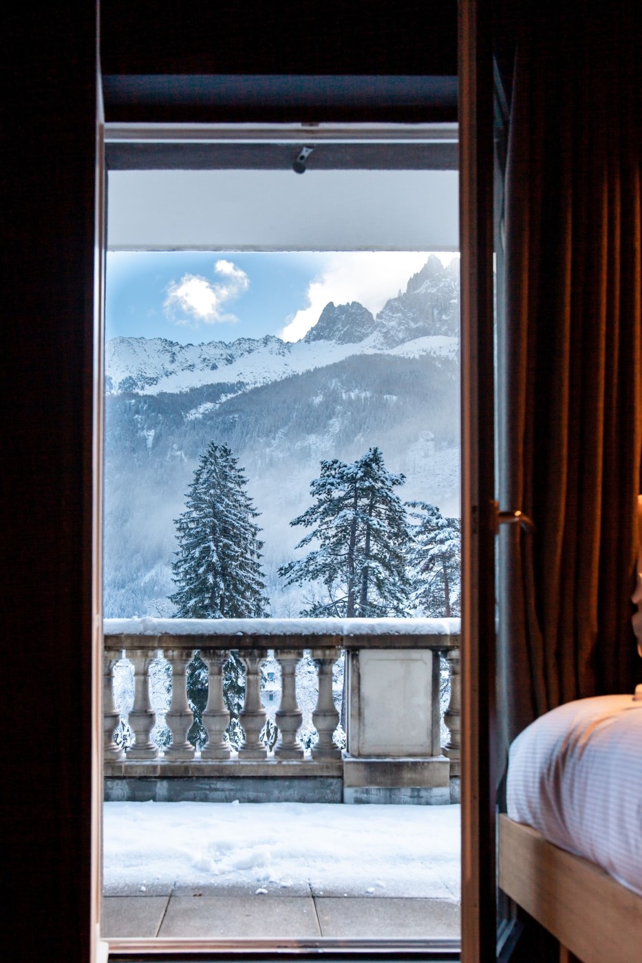 A room with a bed, a window with a view of snow-covered mountains and trees. - La Folie Douce Hôtel Chamonix (Chamonix-Mont-Blanc)