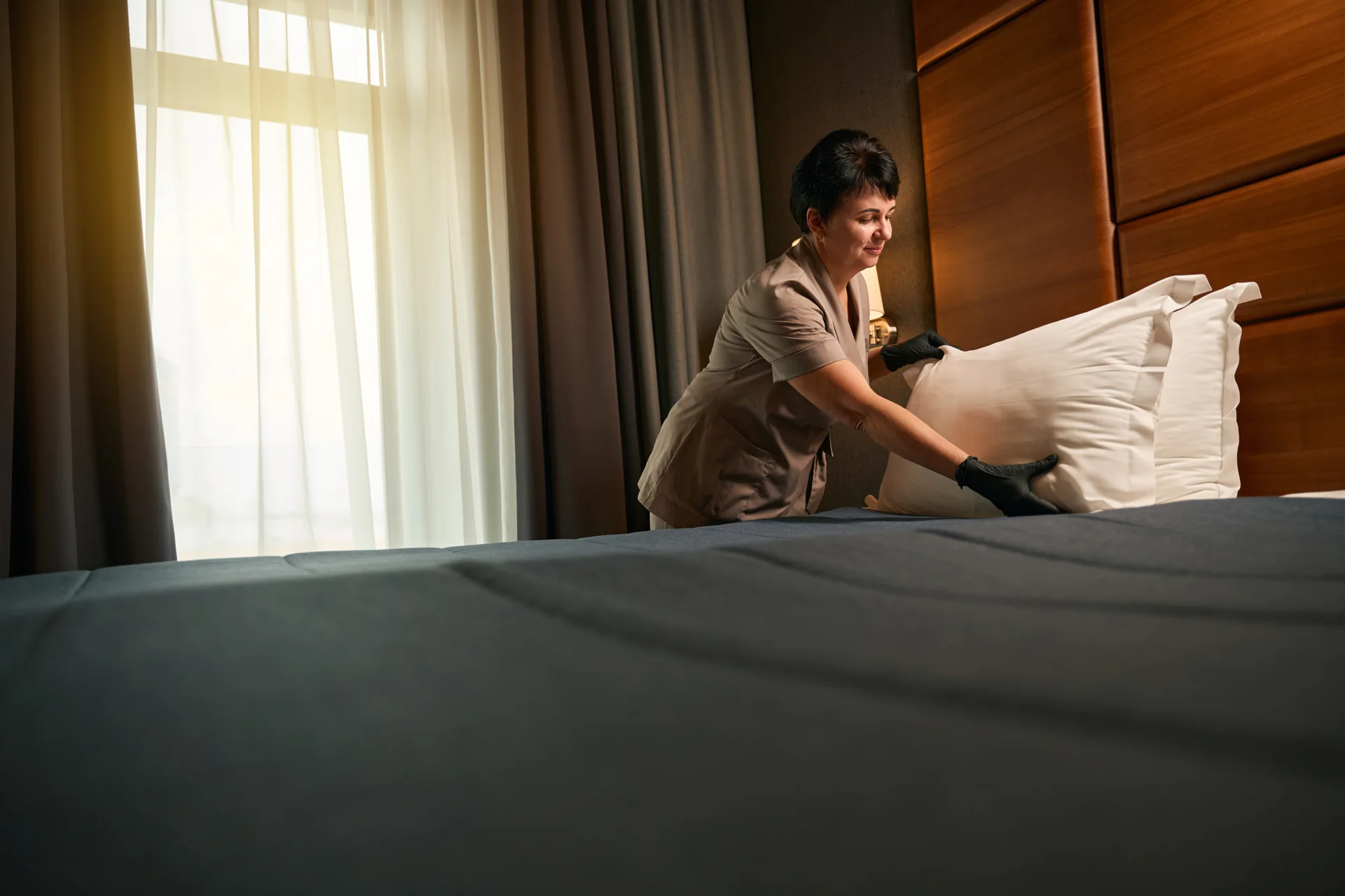 A hotel worker arranging pillows on a bed